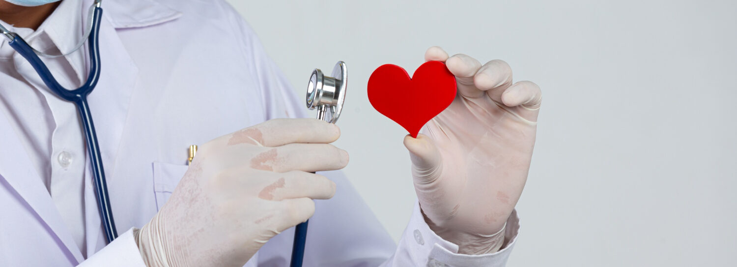 Médico segurando um estetoscópio e um coração vermelho de feltro, simbolizando cuidados com a saúde e prevenção de doenças.